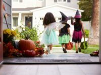 Three Children In Halloween Costumes Trick Or Treating