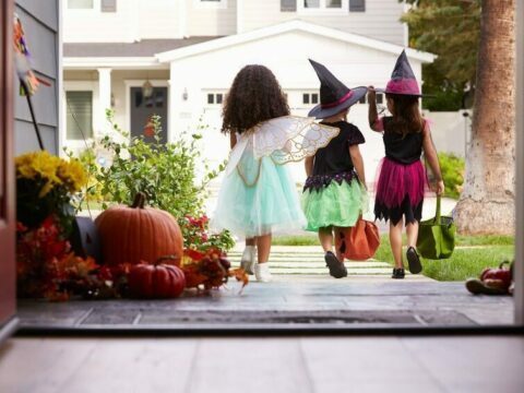 Three Children In Halloween Costumes Trick Or Treating