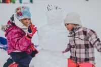 Bild zeigt Kinder beim Spielen mit Schneemann / Outdoor Aktivitäten im Winter mit Kindern